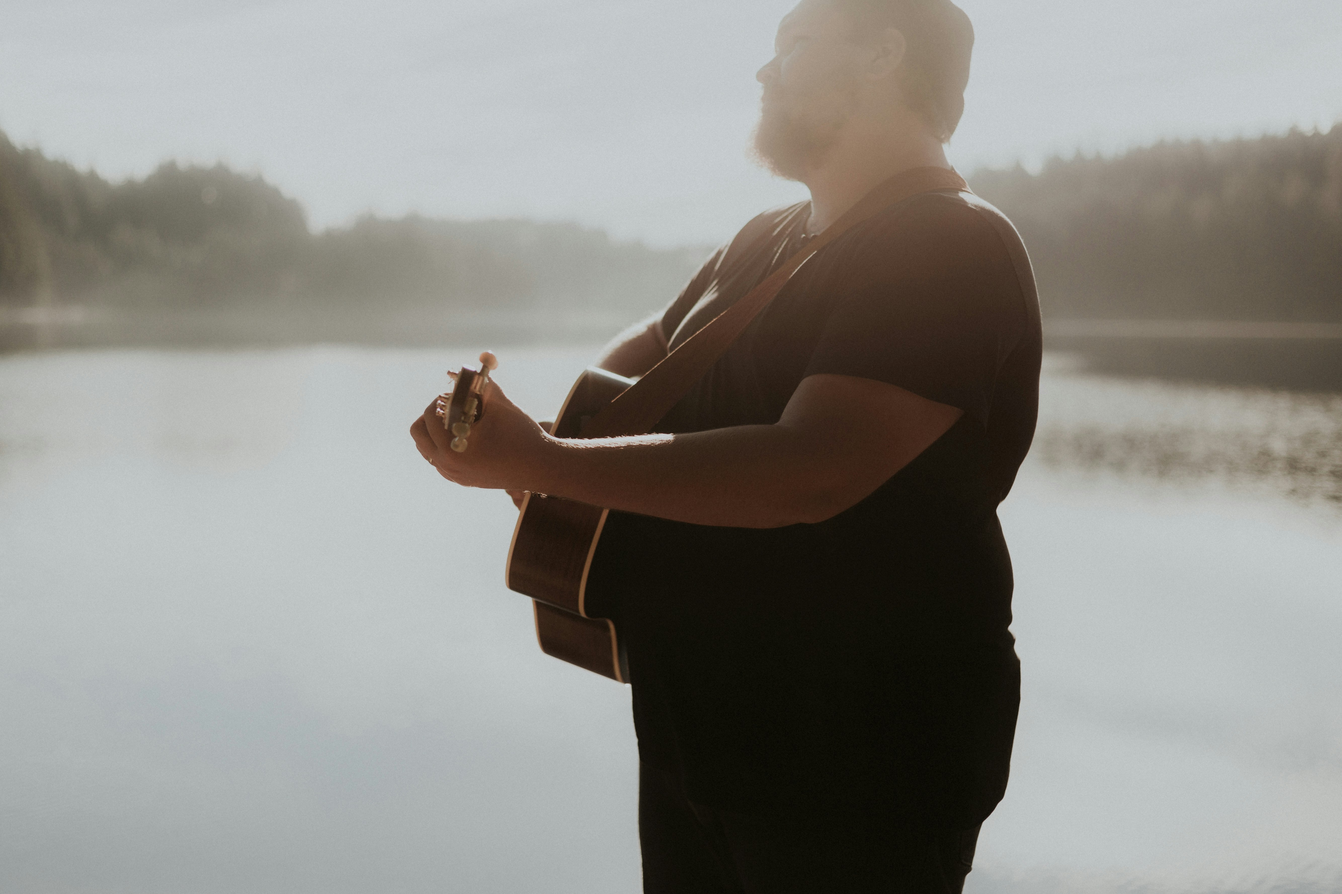 man holding guitar near body of water